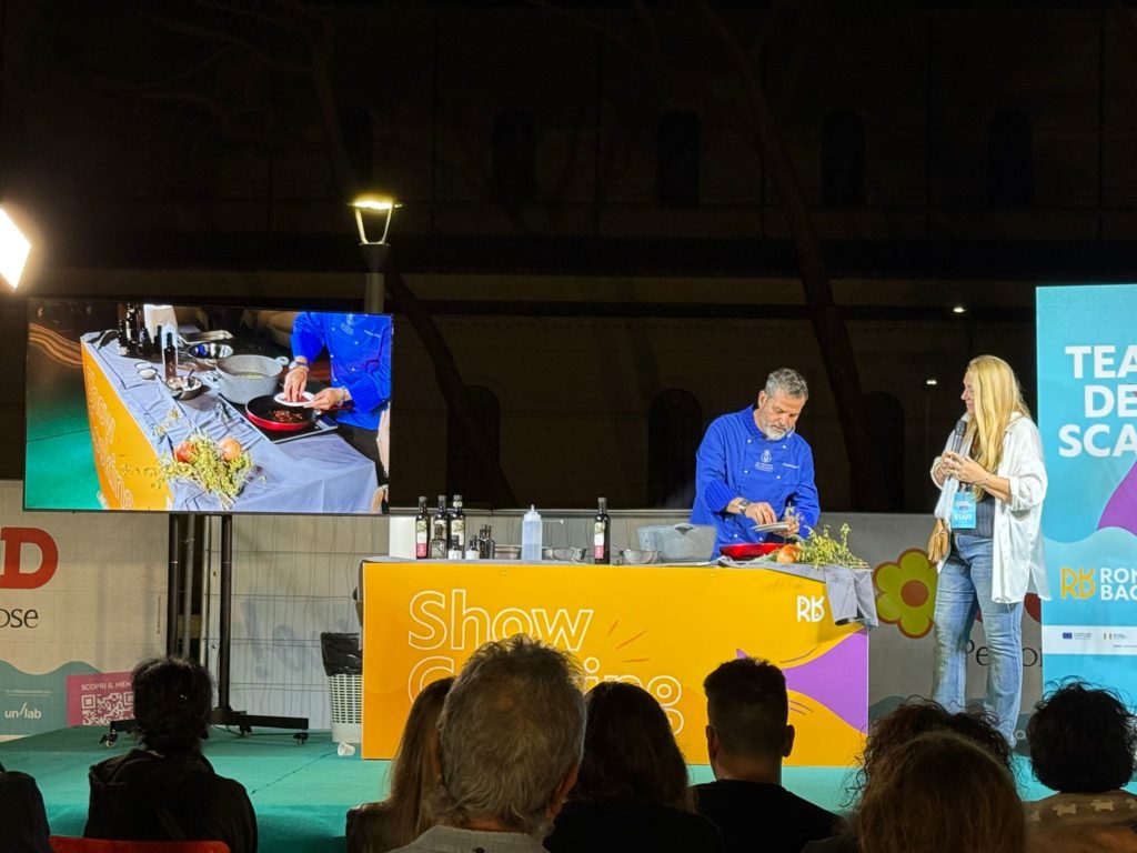 Lo chef ospite prepara un piatto a base di baccalà durante una dimostrazione dal vivo, raccontando tecniche e storie che uniscono gastronomia e sostenibilità.