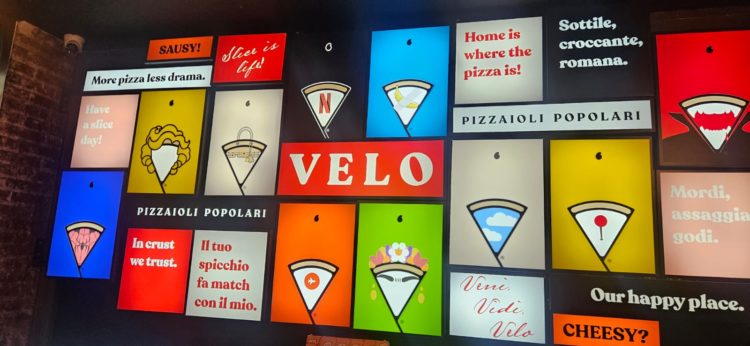 La parete luminosa di Velo con slogan, icone e reinterpretazioni grafiche dello spicchio